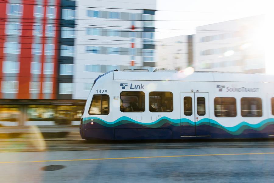 A ground-level light rail train travels at speed in an urban area.