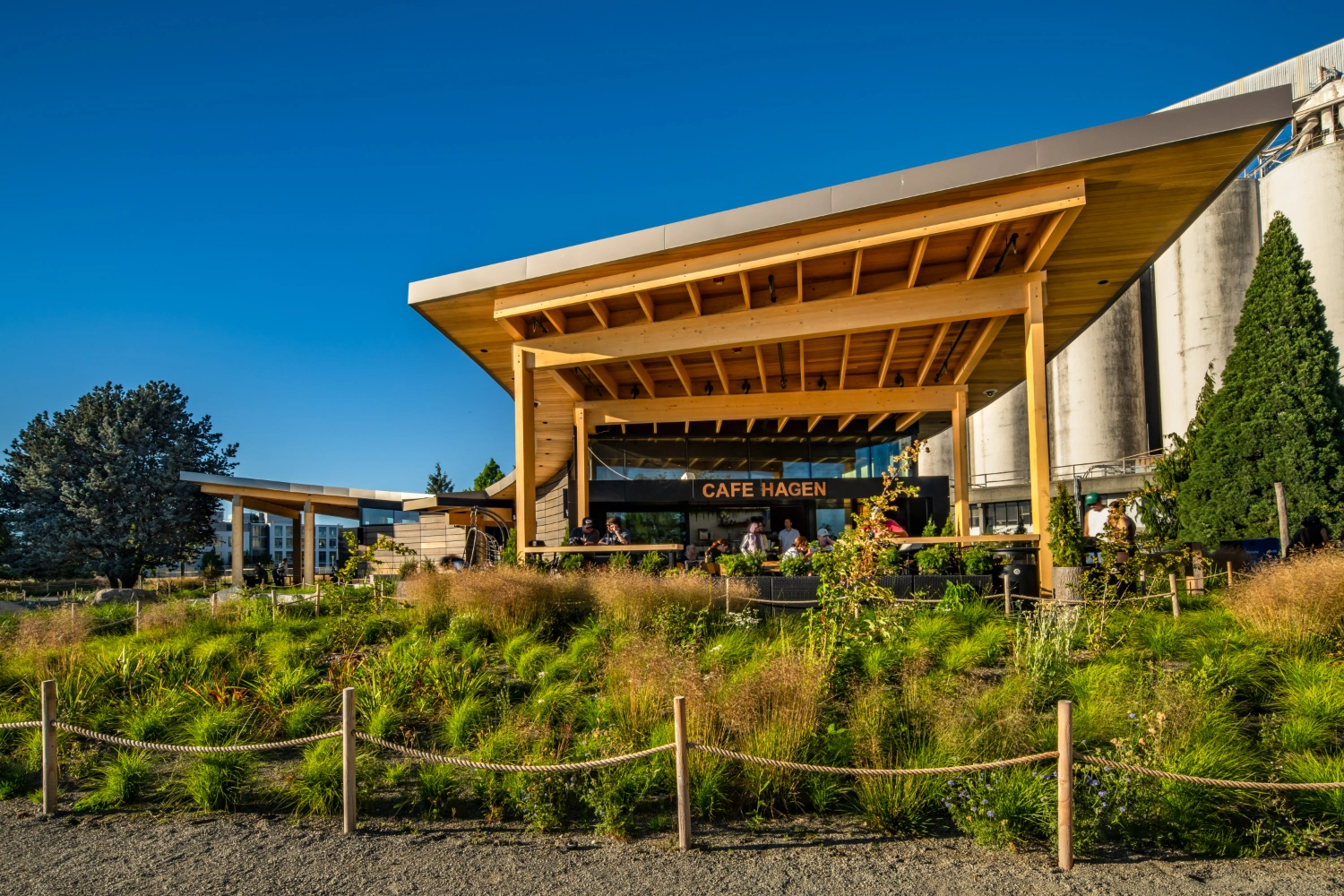 A before and after photo showing a larger amenities building with a curved timber roof that overhangs to create a patio.