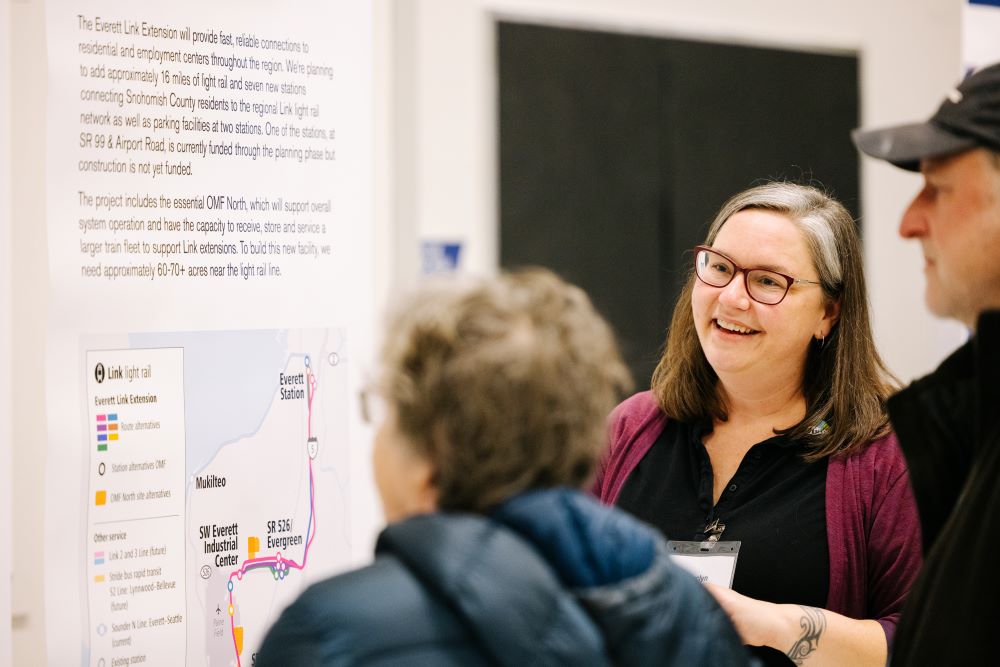 Sound Transit employee smiling while two residents look at a map of the Everett Link Extension project area.