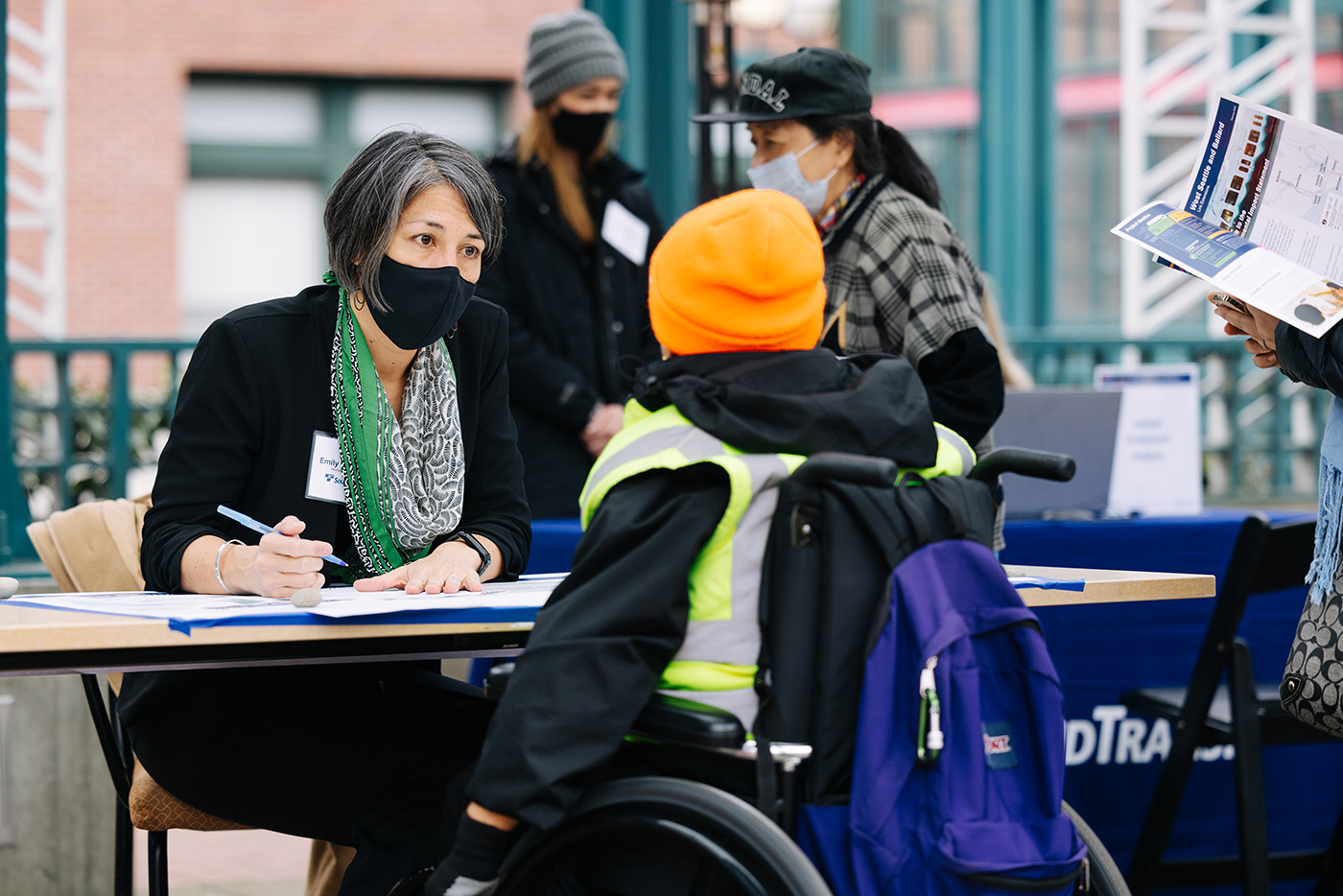 A Sound Transit staff member sits down with a community member outside of the existing Chinatown-International District light rail station to talk to them about the project and write down public feedback.