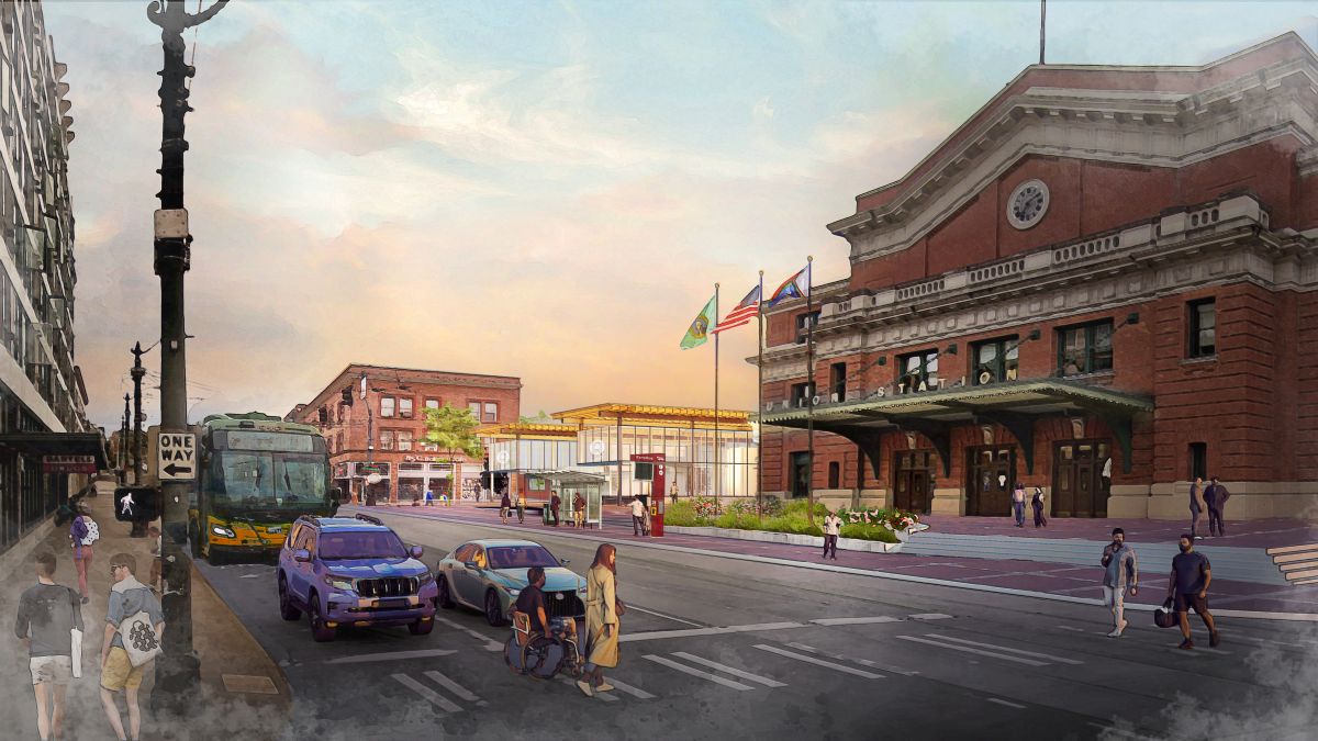 Drawing showing improved plaza, bus stop, and canopy along S Jackson St at the International District Station and Union Station. There are people crossing the street at S Jackson St and 4th Ave S and waiting under a covered bus shelter outside of Union Station.