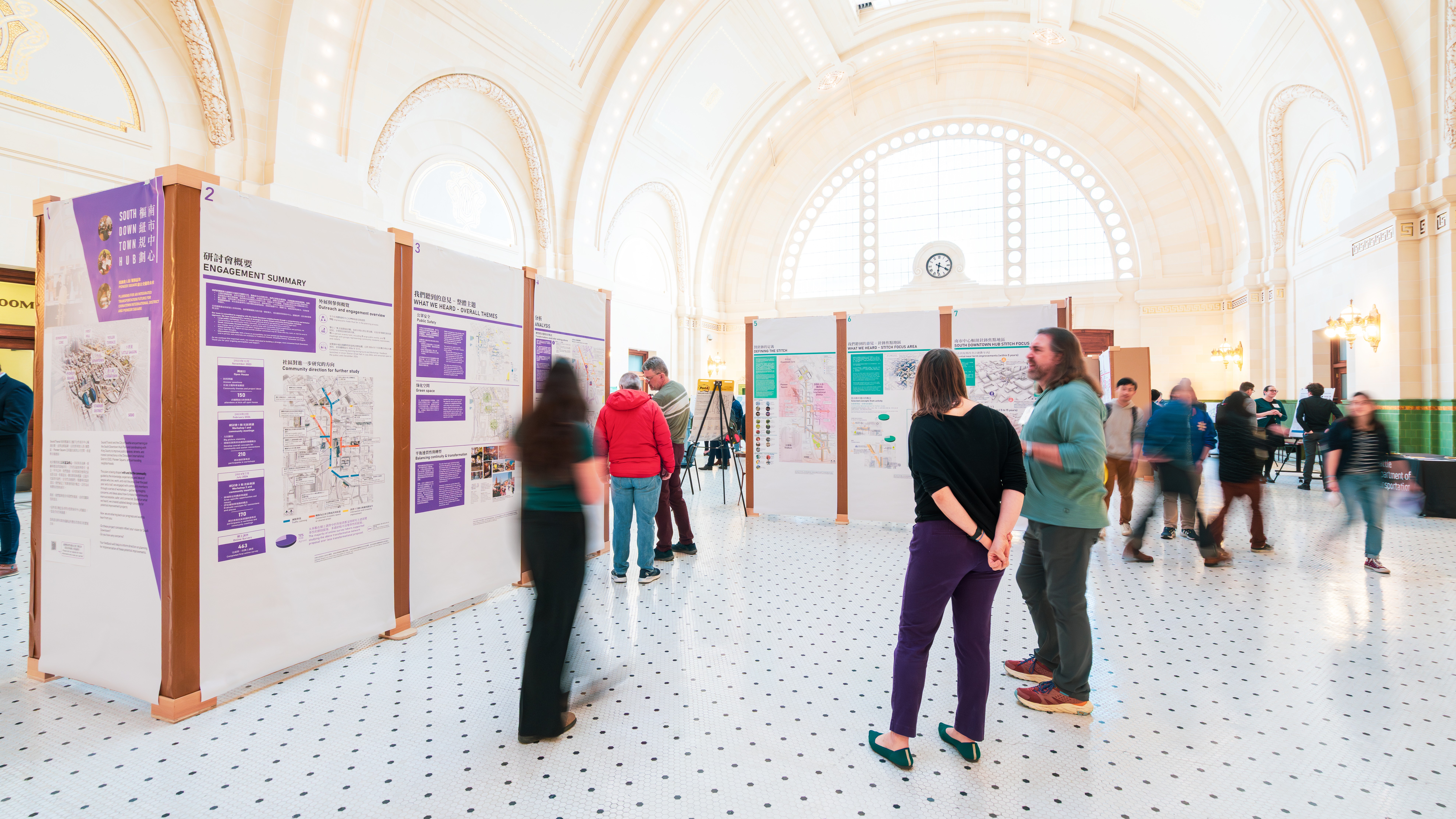 People viewing informational display boards in a large, ornate hall with arched ceilings and natural light. The boards present potential improvement projects, with bilingual English and Traditional Chinese text.